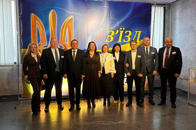 Спільне фото дев’яти учасників з’їзду суддів на тлі банера з гербом України.